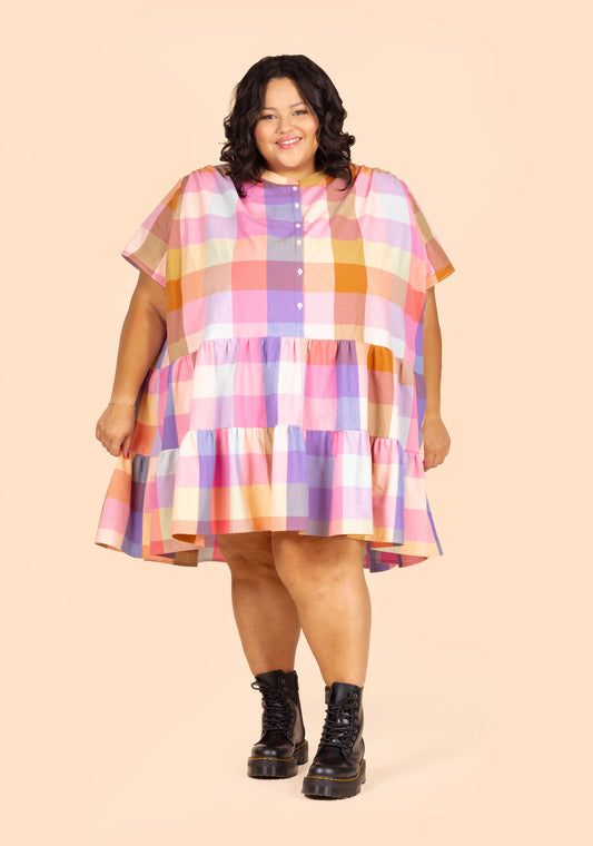 Front standing pose of short Poppy Dress View A in bright plaid cotton, worn with black boots.