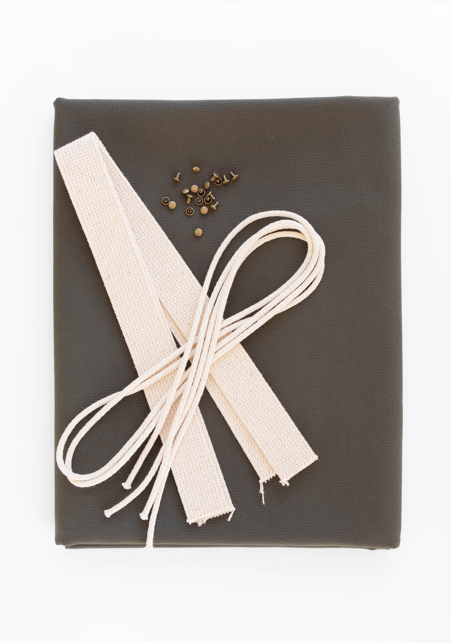 Flatlay of Town Bag fabric kit in pewter green with cotton webbing, drawstring cord, and antique brass rivets.