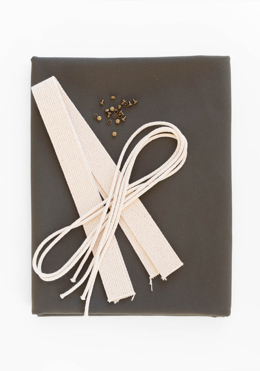 Flatlay of Town Bag fabric kit in pewter green with cotton webbing, drawstring cord, and antique brass rivets.