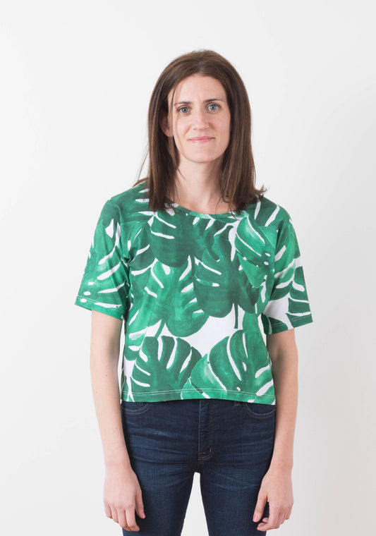 Front view of a woman wearing a short-sleeve Linden Sweatshirt in green monstera print knit fabric.