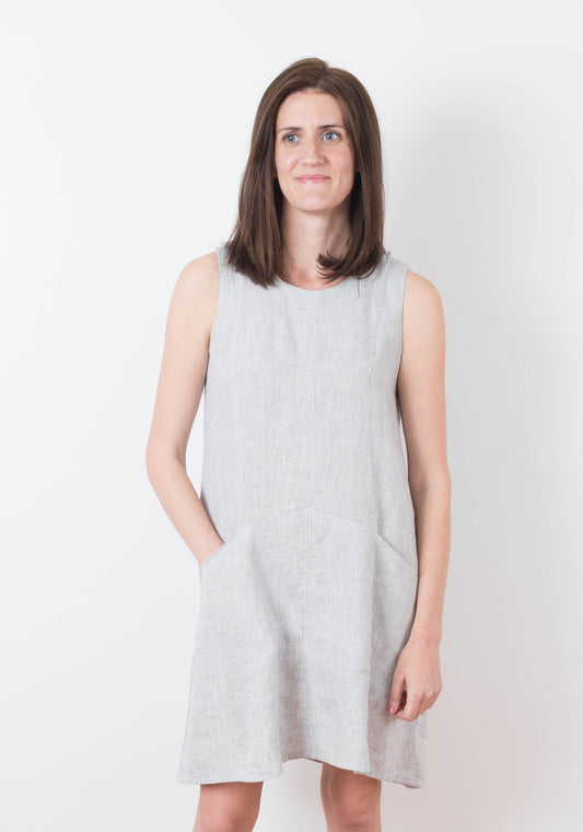 Model wearing sleeveless Farrow Dress in solid light grey fabric with front pockets, view A.