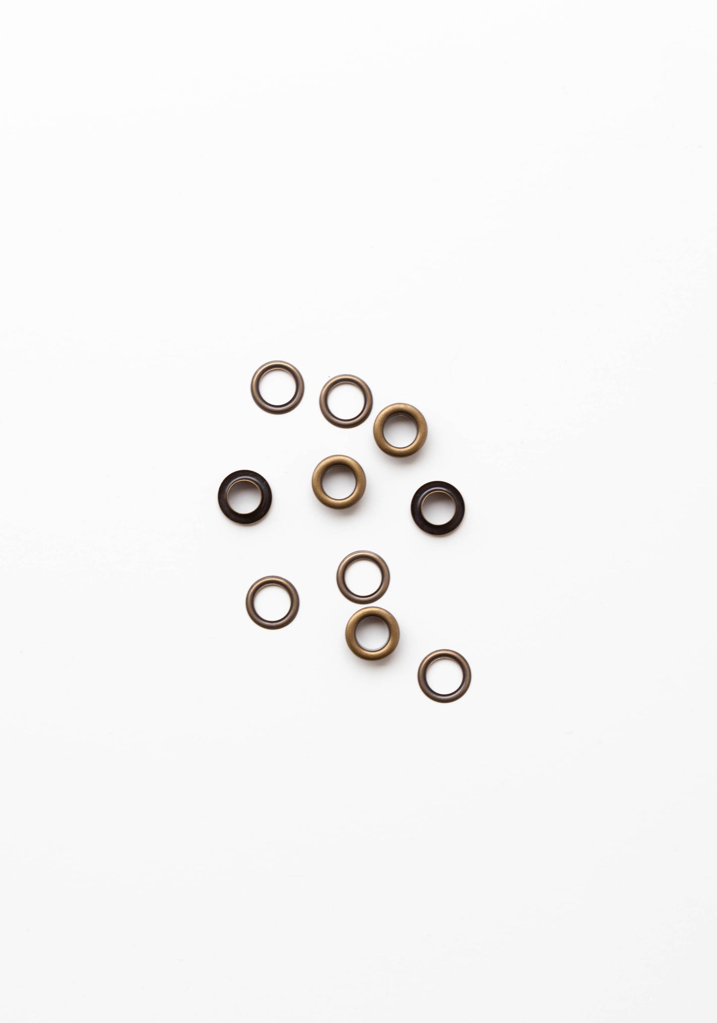 Flatlay of antique brass grommets for the Field Bag sewing pattern on a clean white background.
