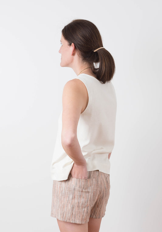 Side view of model wearing striped Grainline Maritime Shorts and ivory sleeveless top, hands in back pockets.