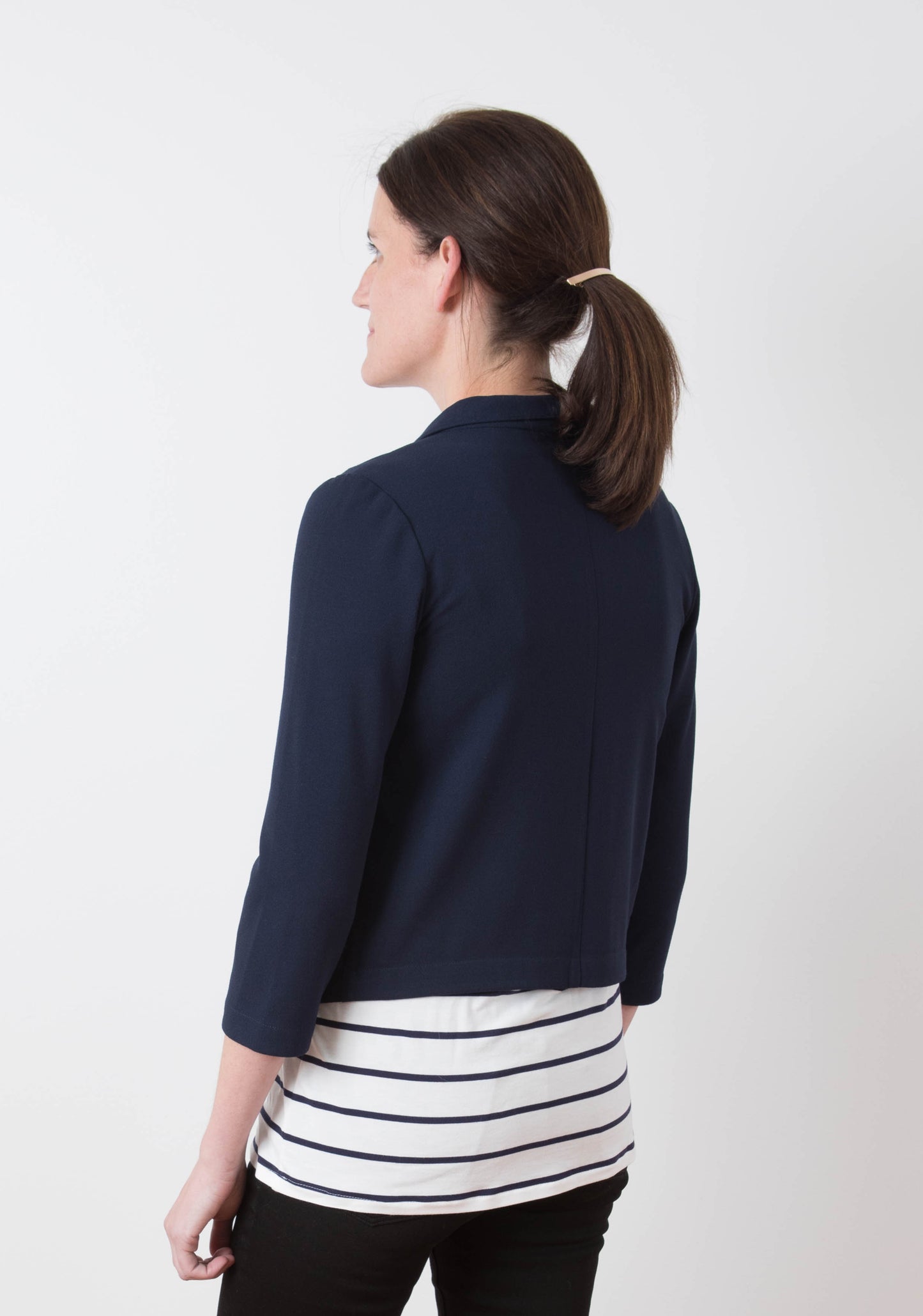 Back view of model wearing Morris Blazer in navy stretch woven fabric with striped tee and black pants.