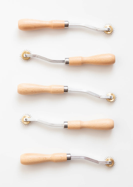 Flatlay of five tracing wheels with wood handles and spiked wheels on white background.