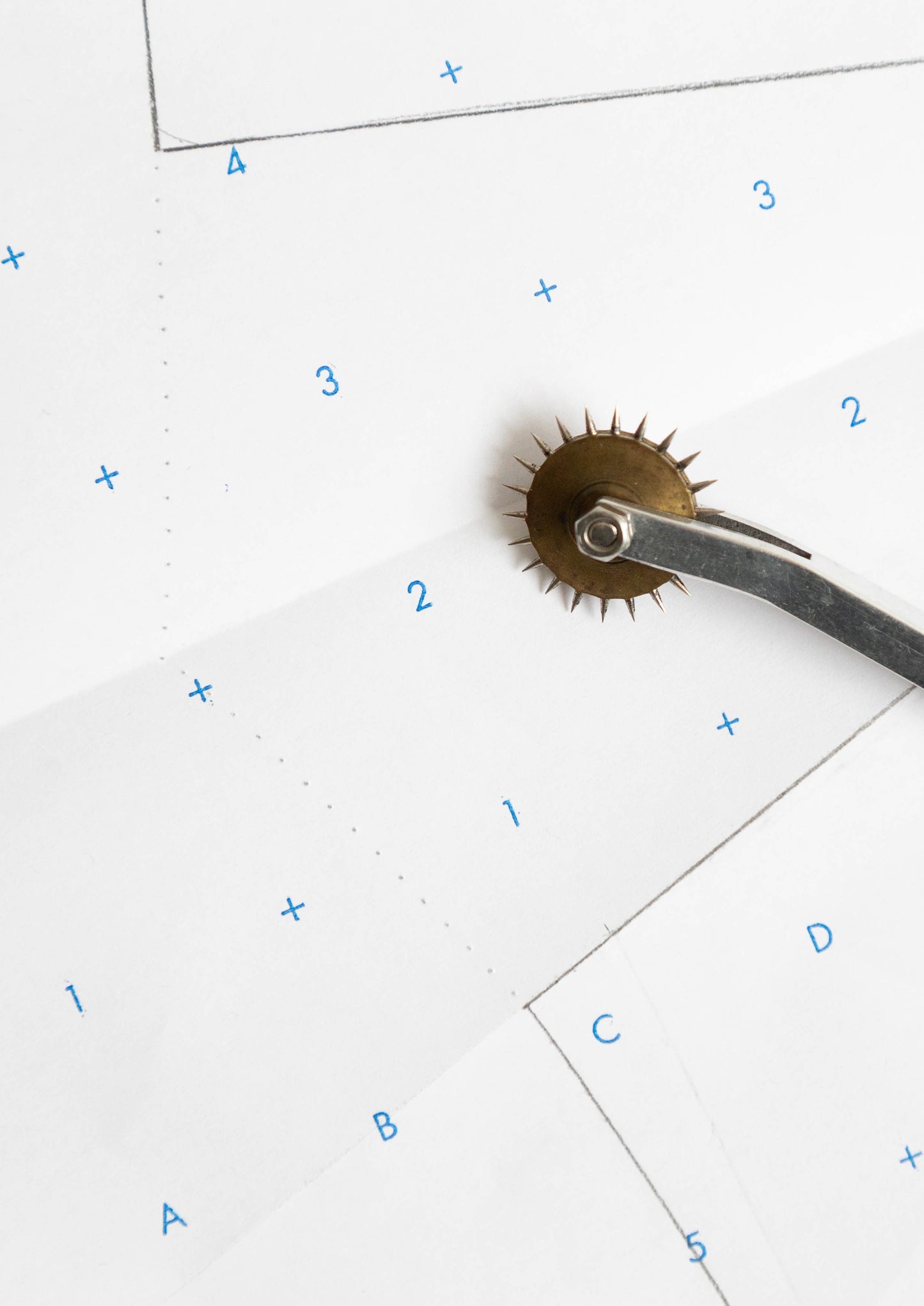 Close-up of tracing wheel creating dotted line along printed sewing pattern grid.