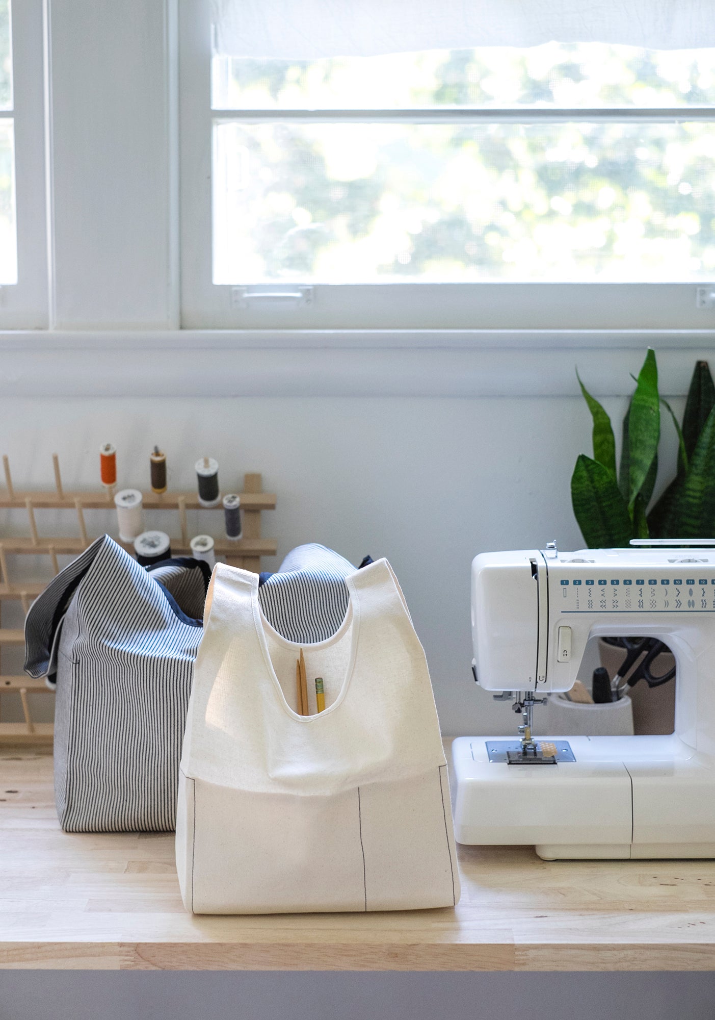 Striped and cream Stowe Bags placed on a sewing table with supplies and a sewing machine.