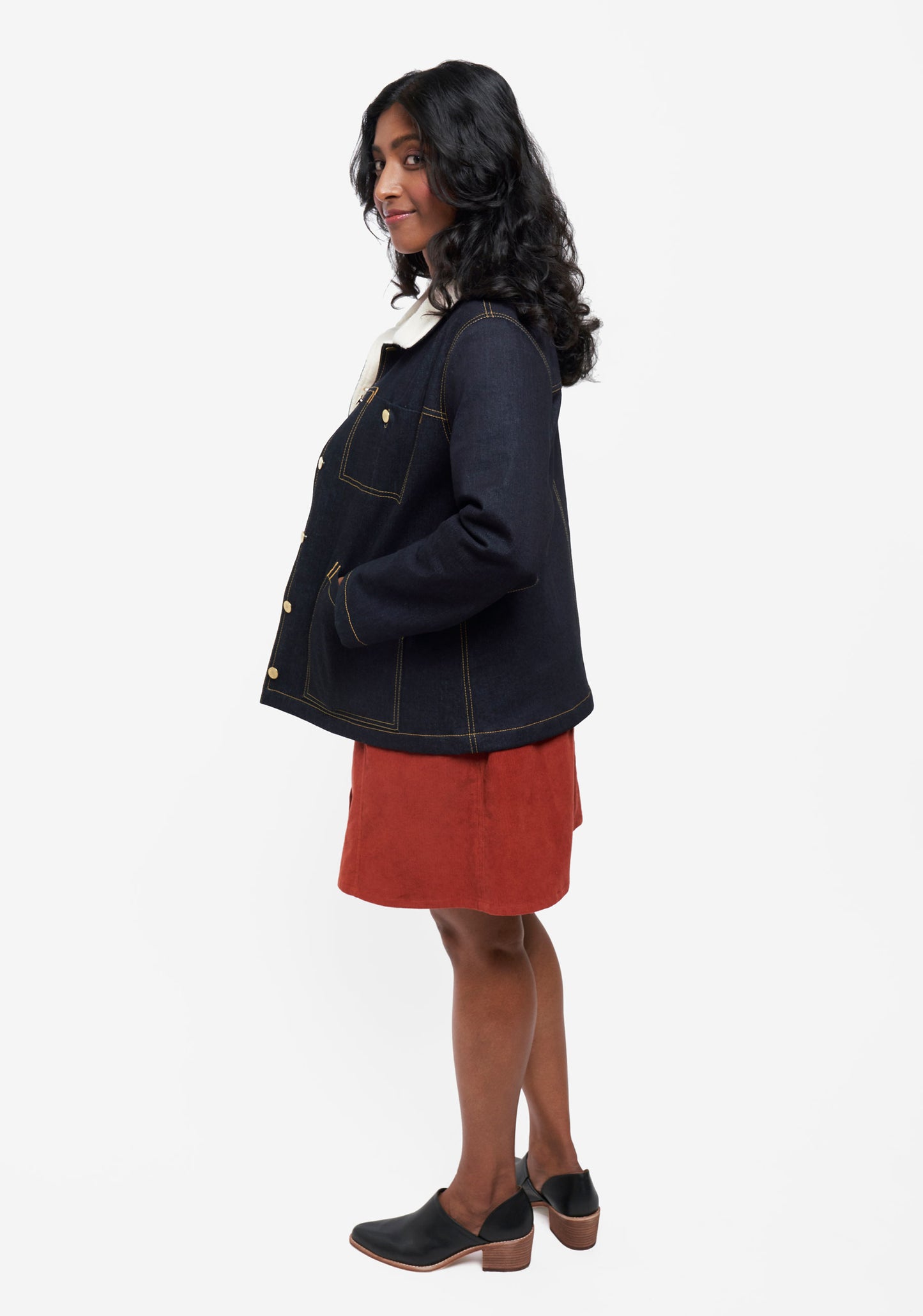 Side view of model wearing Thayer Jacket with rust skirt and black heeled shoes.