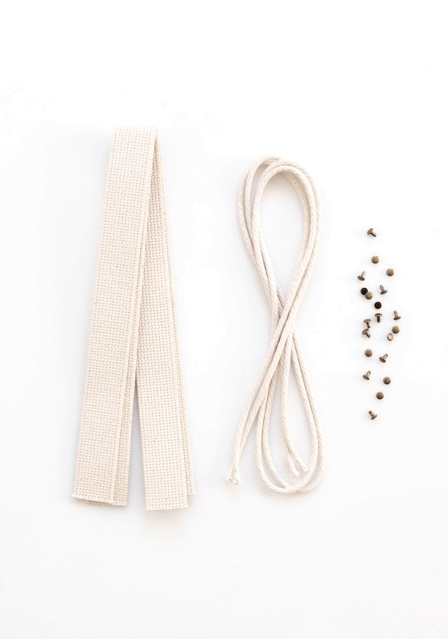 Flatlay of Town Bag Notions Kit showing cotton webbing handles, drawstring cord, and antique brass rivets on white background.