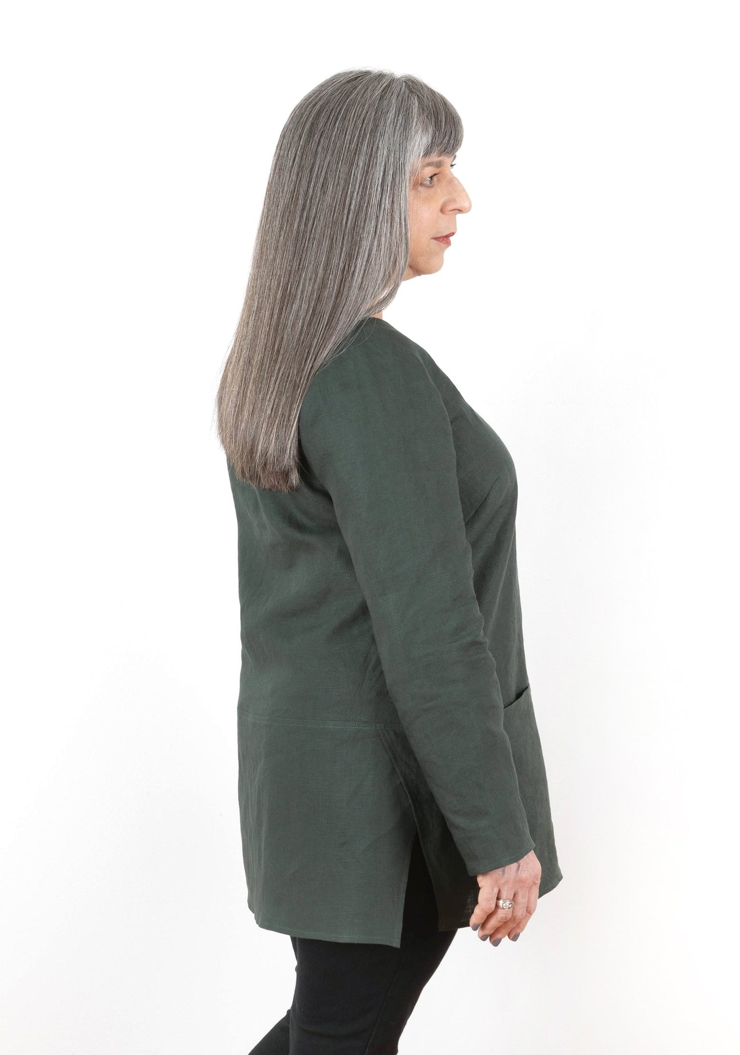 Side view of long-sleeved Uniform Tunic in dark green linen, showing inseam pockets and overlapping side split.