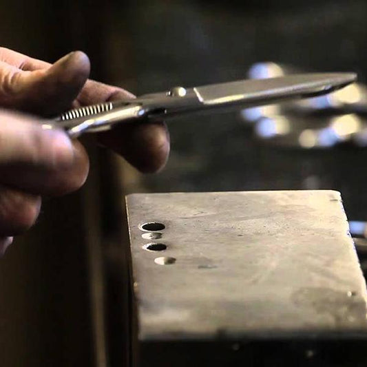 Close-up of hands holding handcrafted scissors above wooden block with drilled holes showing traditional scissor-making technique