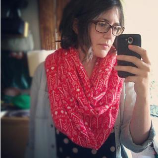 Person taking a mirror selfie wearing a red and white arrow print infinity scarf with a denim shirt and polka dot top