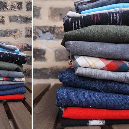 Two stacks of folded garments in woven and knit fabrics including plaids, stripes, and solids in navy, red, gray, and olive