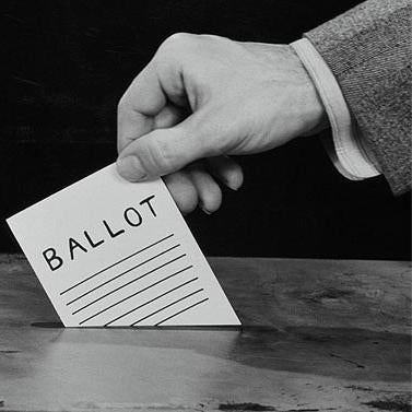 Black and white photograph of a hand inserting a ballot into a voting box
