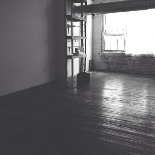 Empty loft studio in black and white with hardwood floors, exposed brick, wooden shelving, serger, and a cased sewing machine
