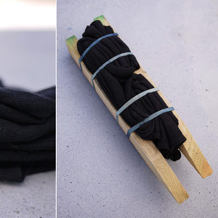 Black fabric bundled with wooden sticks and rubber bands demonstrating shibori resist technique preparation