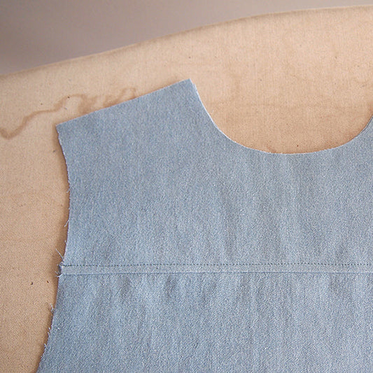 Alder Shirtdress light-wash denim back yoke seam with a single row of topstitching, laid flat on an ironing board