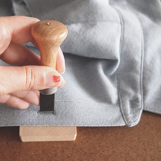 Hand using a wooden buttonhole chisel and cutting block to cut a buttonhole in light gray Alder Shirtdress fabric