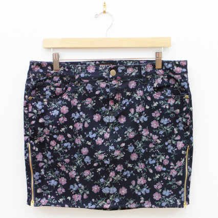 Navy floral mini skirt with pink and blue flowers and gold side zippers displayed on a wooden hanger