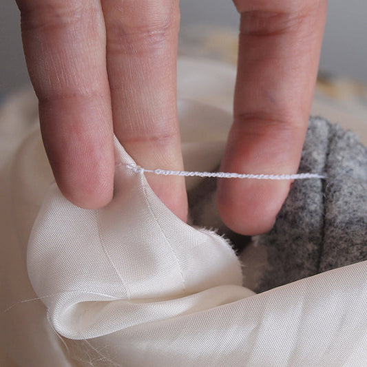 Close-up of hands demonstrating a thread chain, connecting white lining to gray wool with a hand-crocheted thread chain