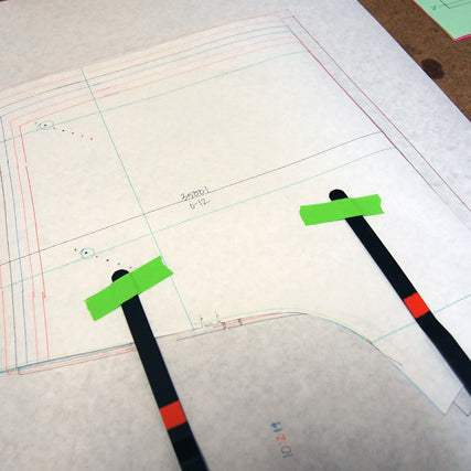 Sewing pattern pieces for Maritime Shorts pinned to tissue paper with green tape and black markers for pattern matching