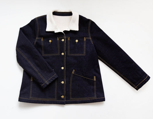 Thayer Jacket in dark indigo denim with cream sherpa collar, gold topstitching, patch pockets, and gold buttons, laid flat