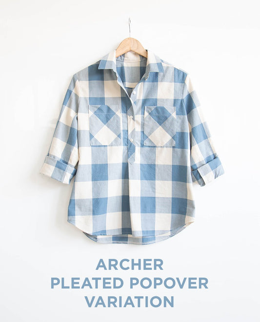 Archer Pleated Popover variation in blue and cream buffalo check with dual chest pockets and rolled sleeves on a wooden hanger