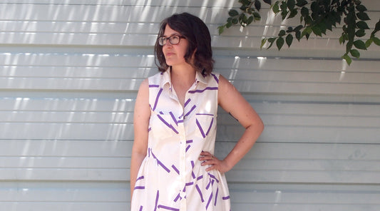 Woman wearing a sleeveless Alder Shirtdress in cream silk twill with purple geometric print, with collar and chest pocket