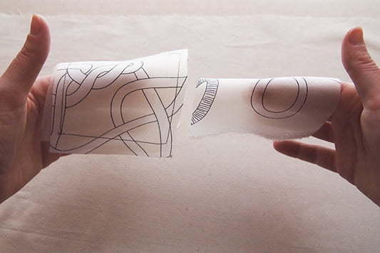 Two hands holding fabric swatches side by side, comparing interfaced and non-interfaced lightweight silk for sewing