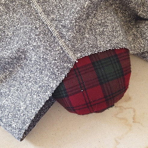 Close-up of a gray woven Linden sweatshirt raglan sleeve folded over a red tartan tailor's ham for pressing