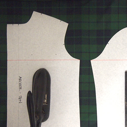 Archer Button-Up pattern pieces on green plaid fabric with a red line marked across underarm points for plaid matching
