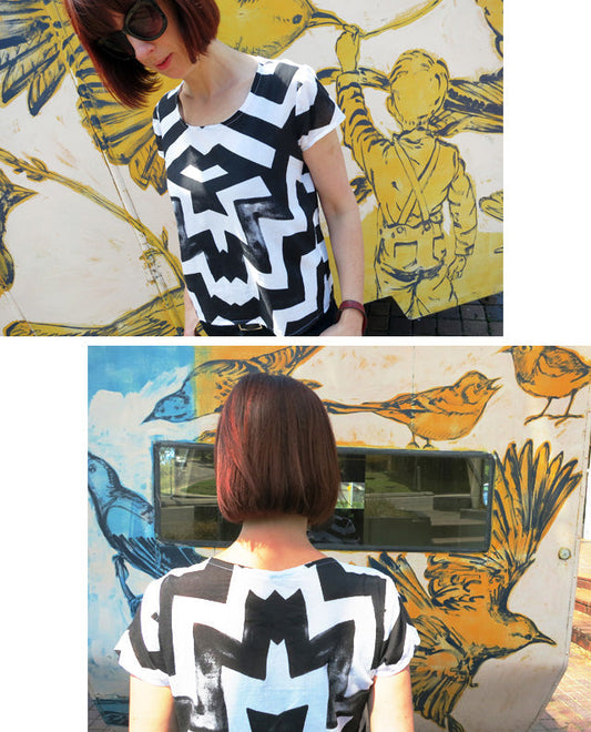 Front and back views of a Scout Tee in black and white geometric print against a street mural with yellow and blue birds