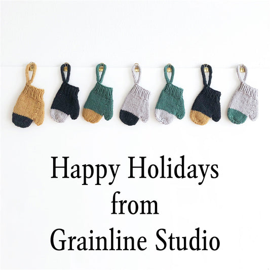 "Happy Holidays from Grainline Studio" with seven colorblock handknit mitten ornaments clipped to a line