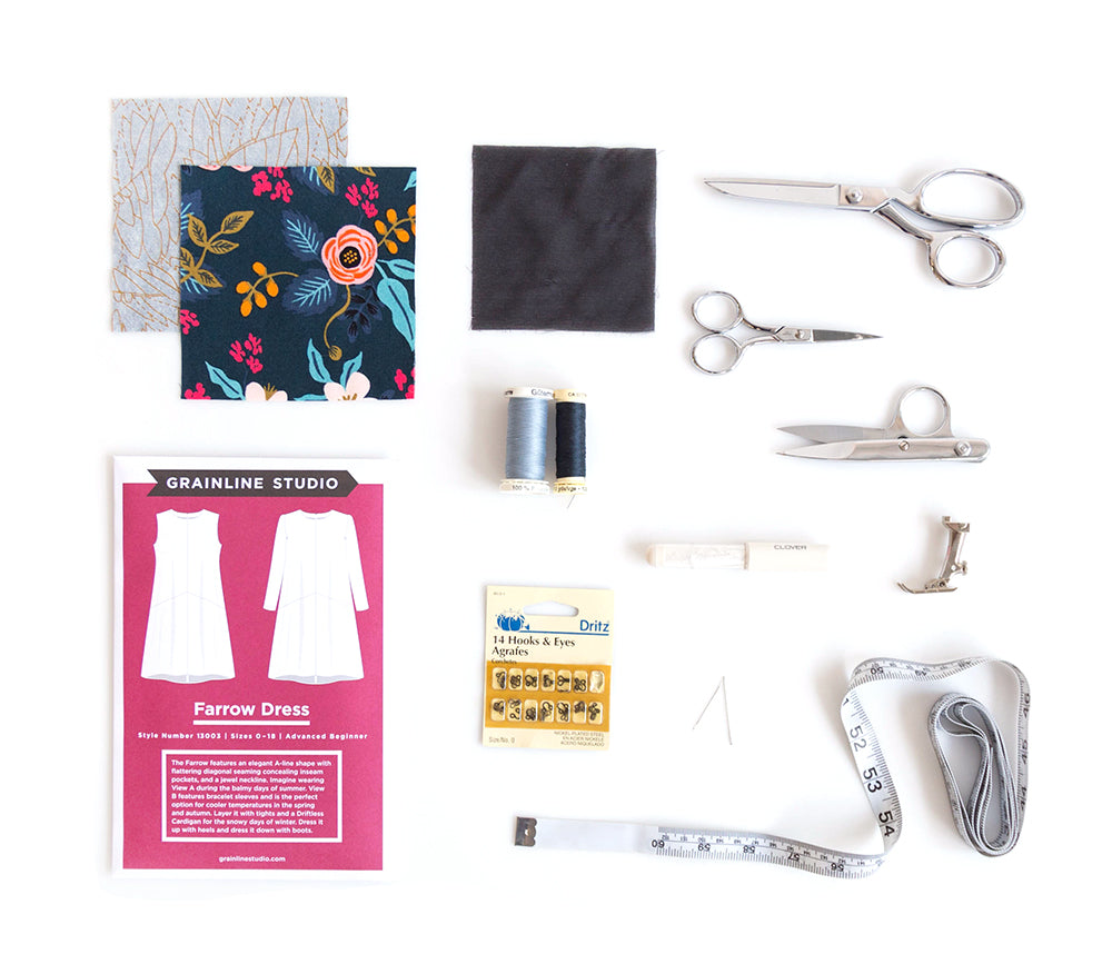 Flat lay of Farrow Dress sewing supplies including pattern envelope, fabric swatches, scissors, thread, interfacing, hooks and eyes, and measuring tape.