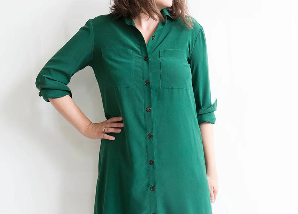 Woman wearing emerald green Archer-Alder hybrid dress with rolled sleeves, breast pockets, and button front closure