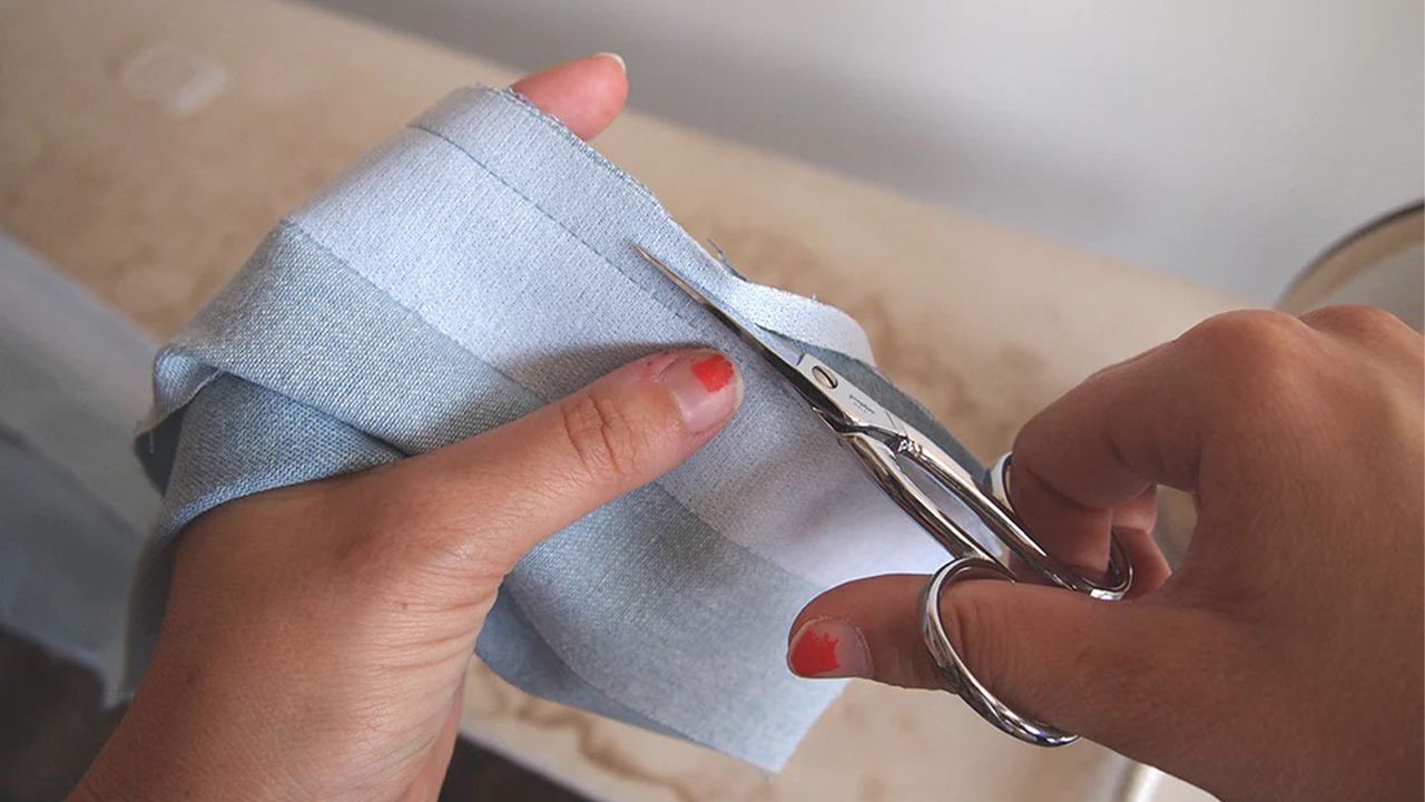 Hands using embroidery scissors to grade seam allowance on light blue denim Alder button band