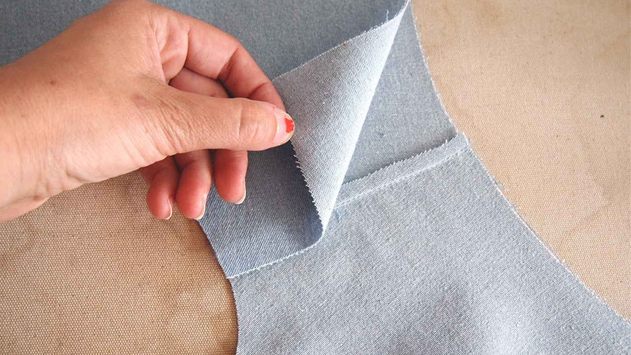 Hand lifting inner yoke piece on gray denim Alder showing graded seam allowances at shoulder seam attachment point