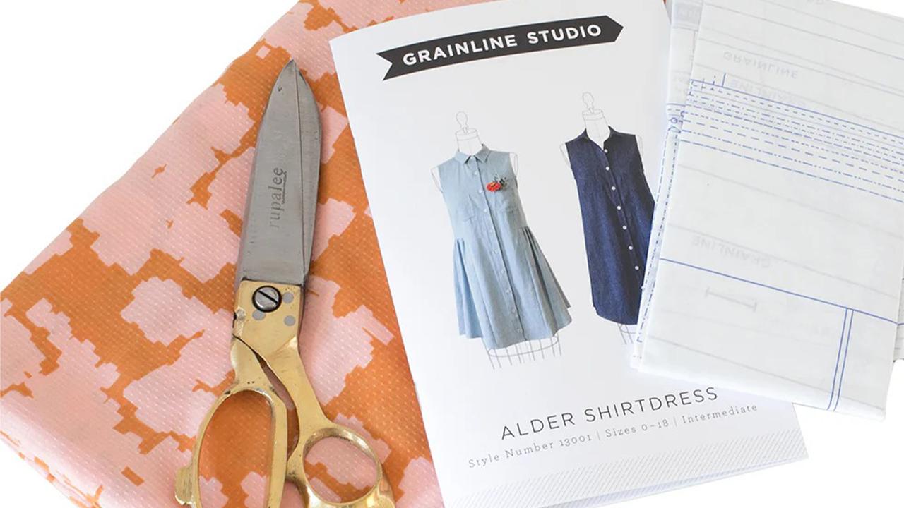 Alder Shirtdress pattern envelope with scissors and coral abstract print fabric on white surface with pattern pieces visible