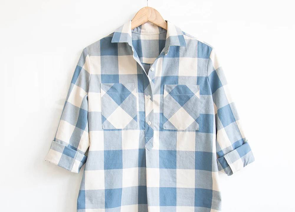 Blue and cream buffalo check Archer Popover on a wooden hanger with bias-cut pockets and rolled sleeves.