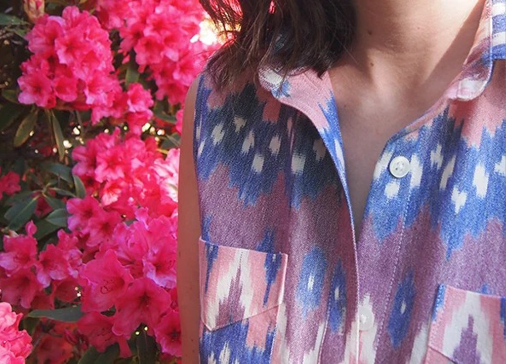 Close-up of a sleeveless pink and blue ikat Archer with a folded triangle flap on each pocket beside pink rhododendrons