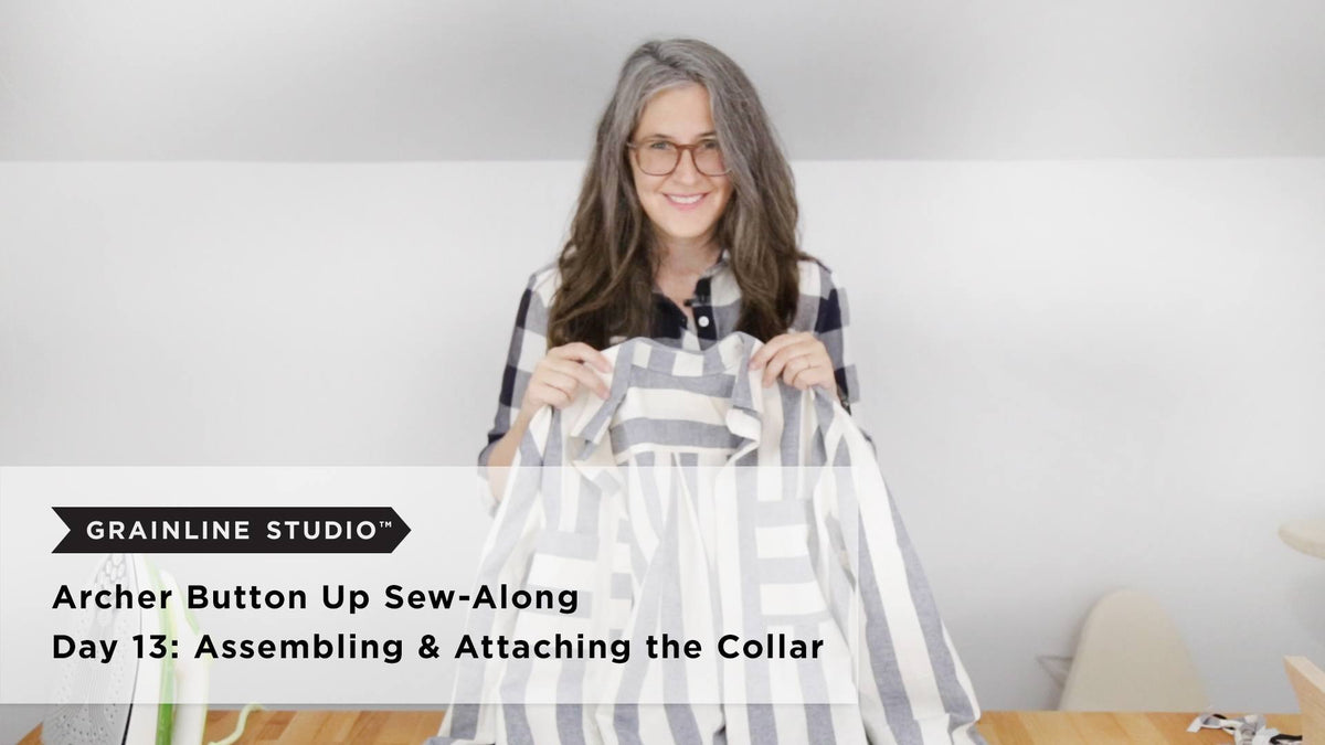 Woman smiling and holding up a gray and white striped Archer shirt with its collar attached, beside an iron