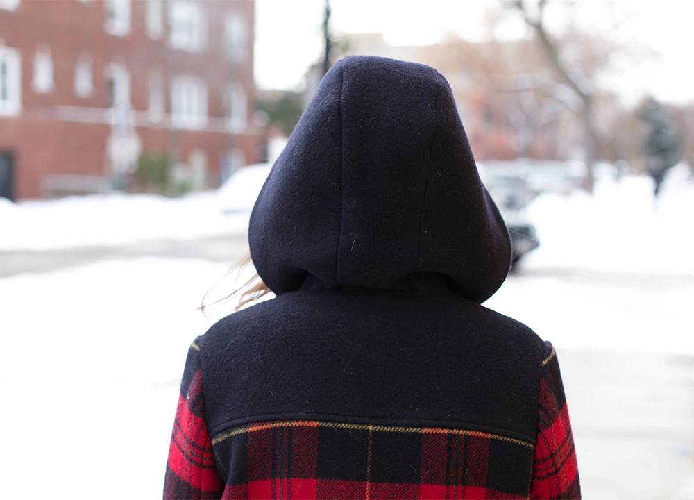 Back view of Cascade coat with navy hood and yoke contrasting with red plaid body worn outdoors in snowy setting