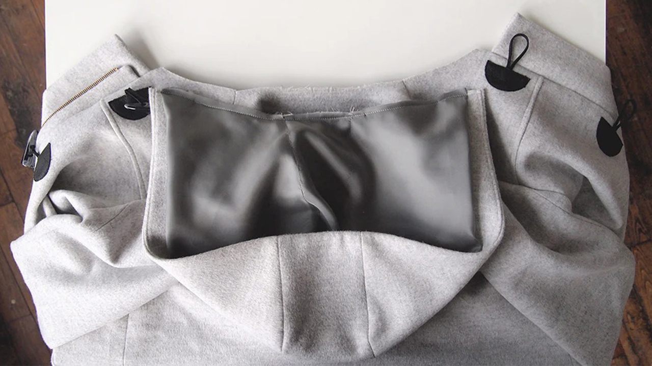 Completed hood laid flat showing gray wool exterior with black Bemberg lining and toggle closures visible at sides