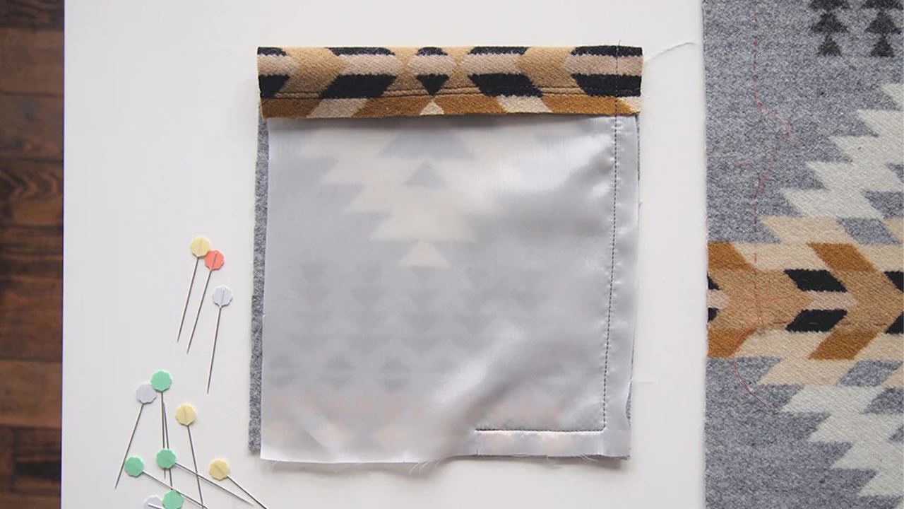 Completed patch pocket with gray lining on geometric print wool coating, topstitched edges and colorful pins nearby