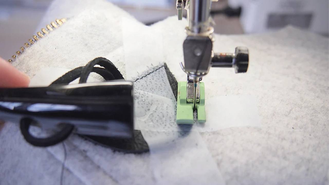 Sewing machine with green Teflon foot stitching black leather toggle tab to gray wool coat fabric