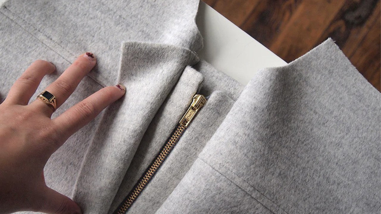 Hand positioning zipper band layers on gray wool coat showing brass separating zipper sandwiched between fabric bands