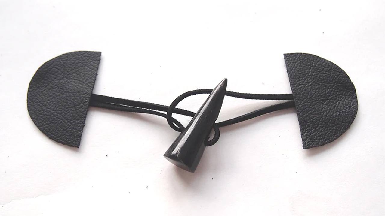 Completed toggle closure with black leather tabs connected by black cord threaded through black toggle button on white surface