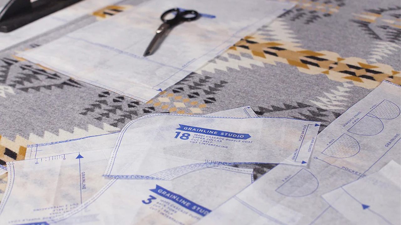 Cascade Duffle Coat pattern pieces pinned to gray and gold geometric print wool coating fabric with scissors visible