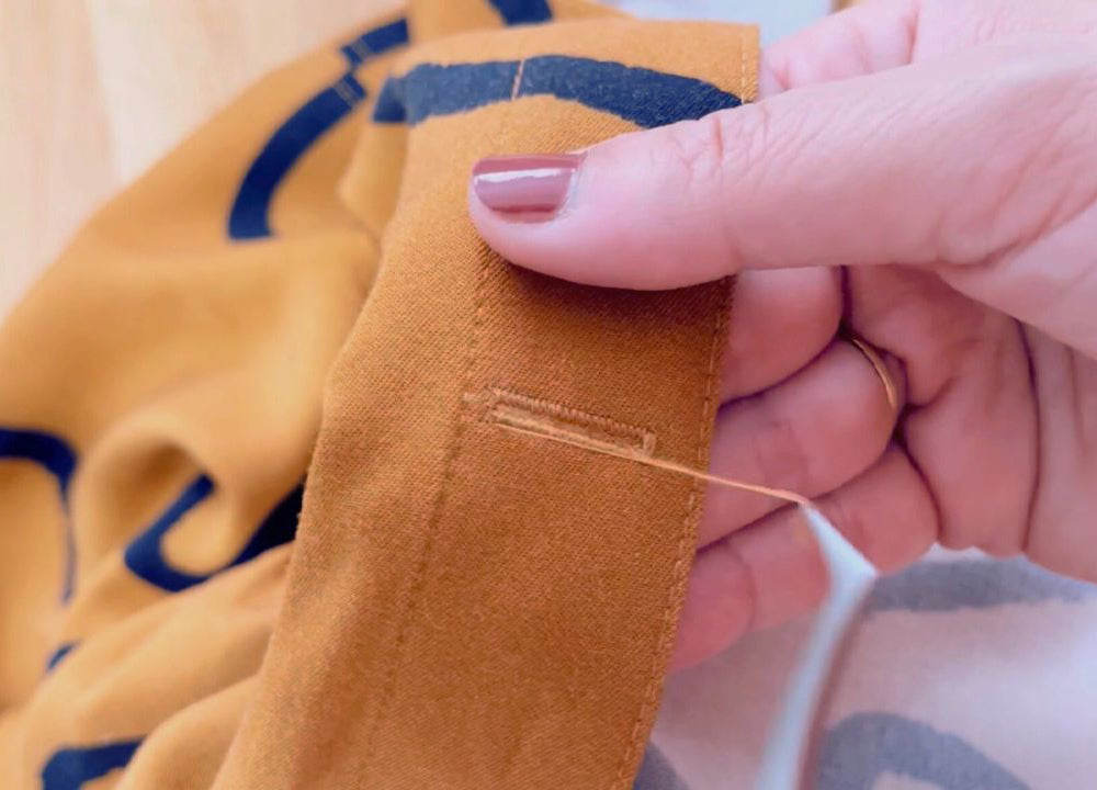 Hand using seam ripper to remove stitched buttonhole on orange twill fabric before cutting open, shown in video tutorial