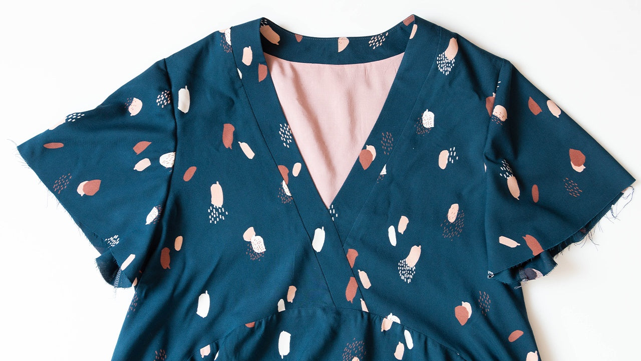 Felix Dress with flutter sleeves in teal abstract print showing faux wrap neckline and pink lining at V-neckline